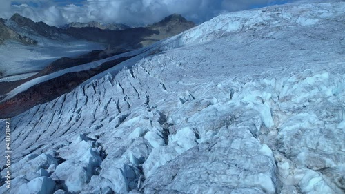 Aerail sideways cinematic icy frozen permafrost glacier on slopes of alpine mountains. Deep cracks, sharp ice tops. Clouds. Glacial period. Climate change, global warming ecology abstract footage 4k