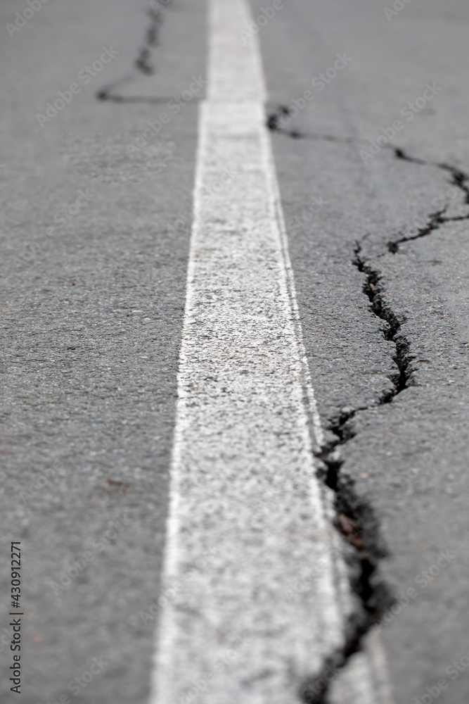 Obraz premium Cracks in the asphalt in the city park. Bicycle path with a white dividing strip. 
