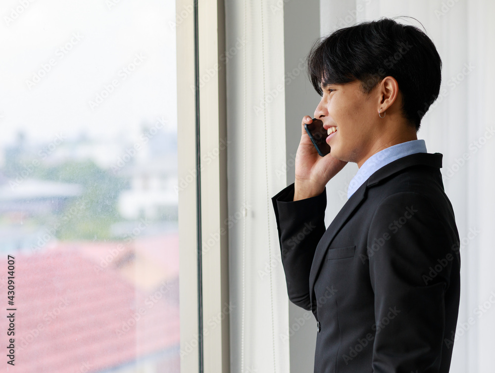 Young and handsome Asian businessman in black suit making call with smarphone Young and handsome Asian businessman in black suit making call with smarphone