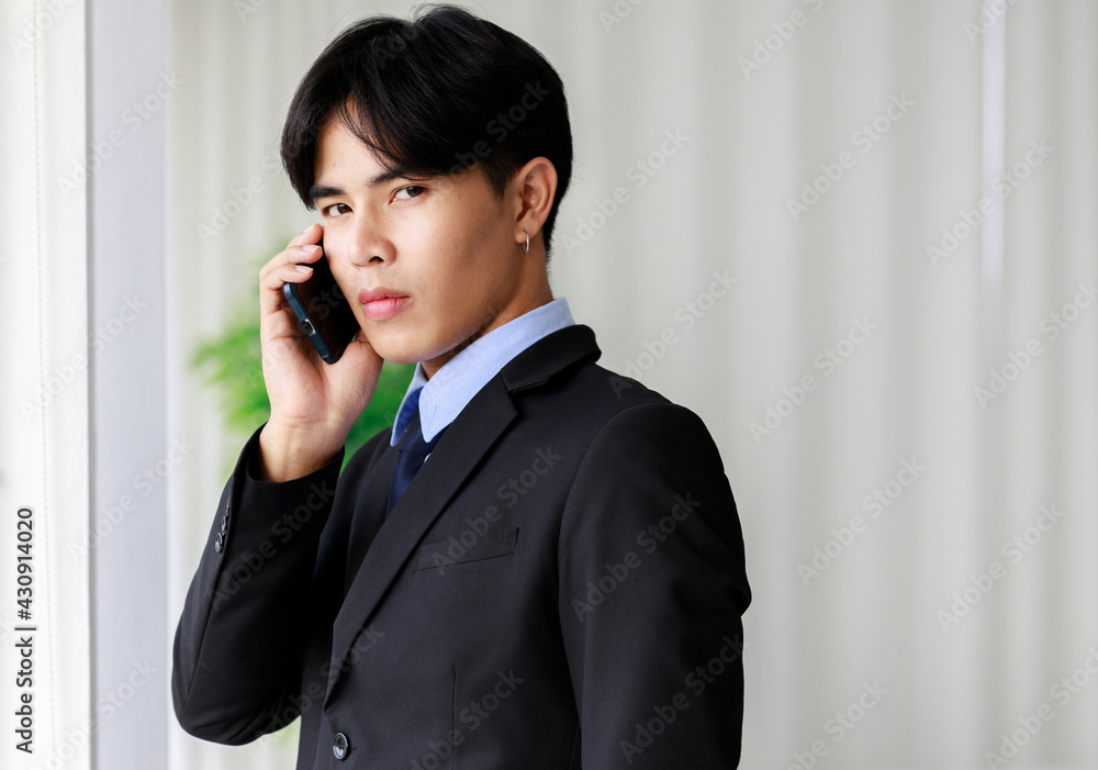 Young and handsome Asian businessman in black suit making call with smarphone Young and handsome Asian businessman in black suit making call with smarphone