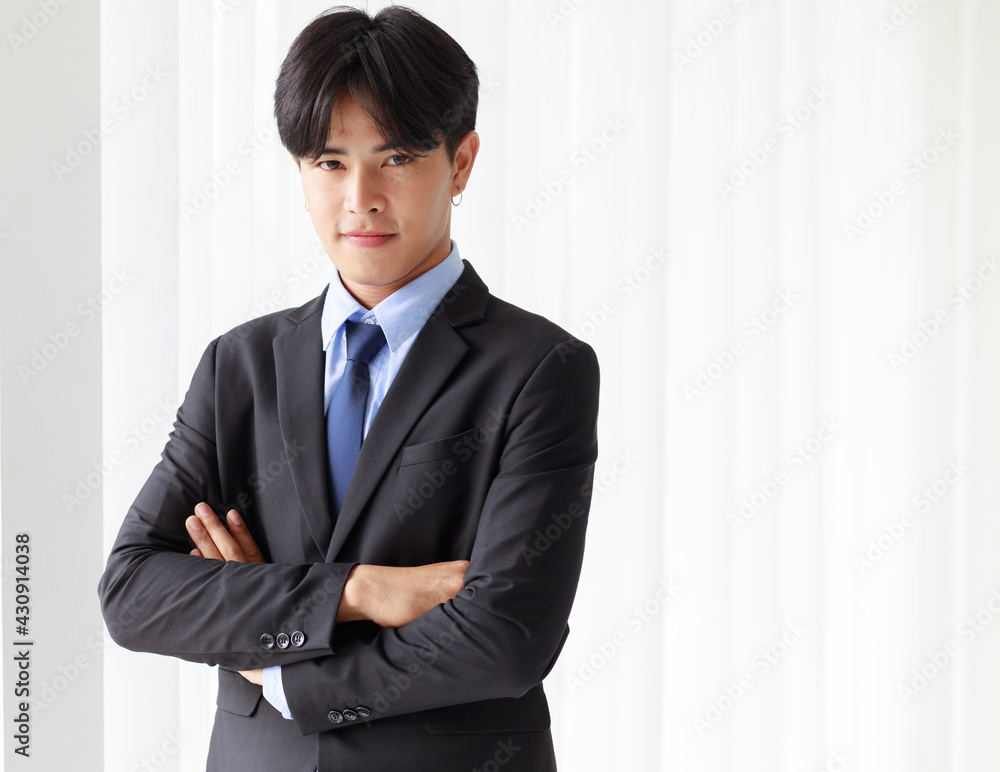 Portrait one young asian businessman who smart and handsome wearing black suit standing look at camera while smiling and folded arms crossed with look feel confident and window on background in office Portrait one young asian businessman who smart and handsome wearing black suit standing look at camera while smiling and folded arms crossed with look feel confident and window on background in office