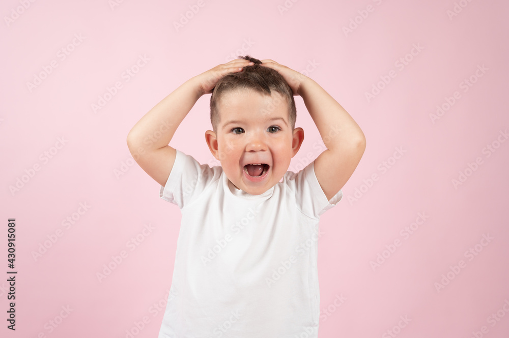 Emotional caucasian little boy grimacing and putting hands to his head, pink surface Emotional caucasian little boy grimacing and putting hands to his head, pink surface