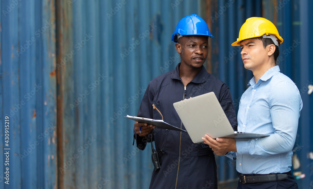 An officer from the Customs Department inspects the cargo in the container yard. Business man in hardhat helmet and African American foreman worker discuss togetherness An officer from the Customs Department inspects the cargo in the container yard. Business man in hardhat helmet and African American foreman worker discuss togetherness
