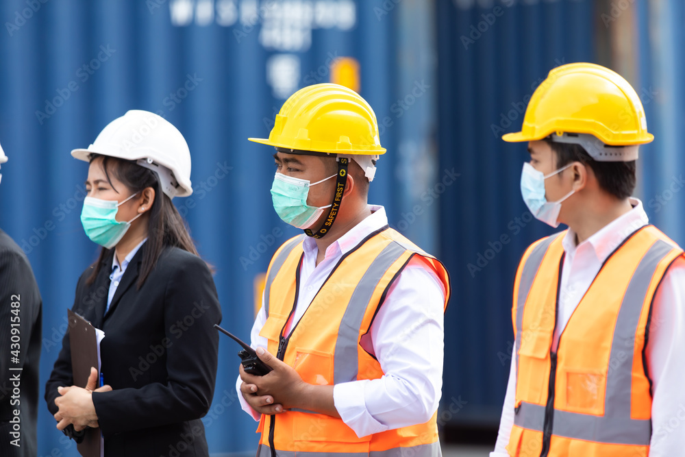 Group of professional team worker wearing protection face mask during coronavirus and flu outbreak and wearing safety hardhat helmet at container yard or cargo warehouse Group of professional team worker wearing protection face mask during coronavirus and flu outbreak and wearing safety hardhat helmet at container yard or cargo warehouse