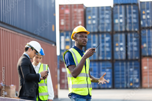 worker talking on walkie-talkie to Colleague at container warehouse at port of import and export goods. African American Industrial factory and energy engineering Specialist.