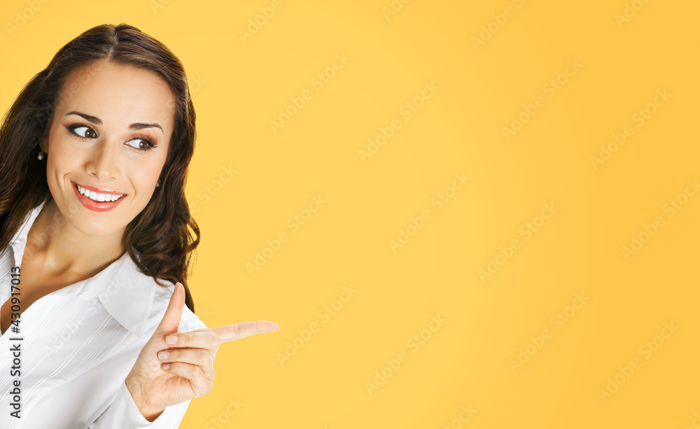 Young happy smiling woman in white confident blouse, showing pointing at copy space. Business concept. Orange yellow color background. Brunette businesswoman. Young happy smiling woman in white confident blouse, showing pointing at copy space. Business concept. Orange yellow color background. Brunette businesswoman.