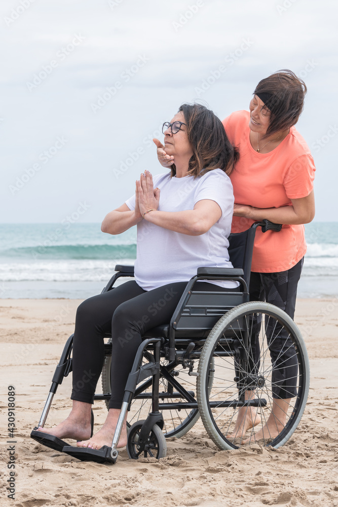 Naklejka premium Mature woman in a wheelchair being helped with her meditation pose: Health and inclusivity concept.