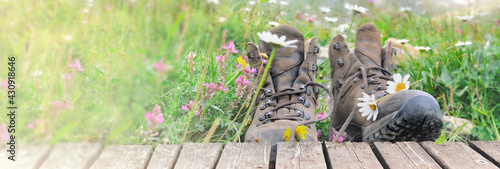 Photos old hiking shoes in a meadow with flowers bloming and a wooden terrace