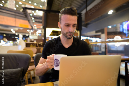 Portrait of handsome man sitting at coffee shop using laptop computer
