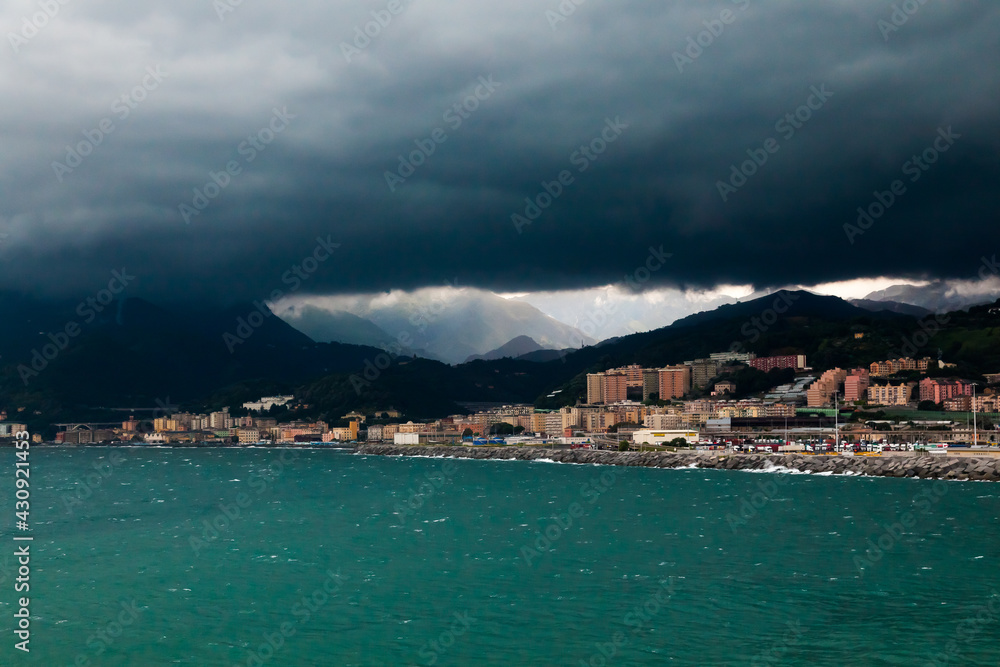 Dark storm clouds over the coast of the city of Genoa, Italy, at the foot of the mountains. Clouds gather over the sea city at the foot of the mountains.