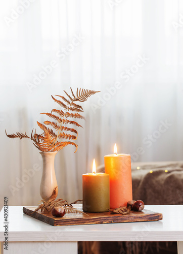 burning candles with autumn decor on white table at home photo