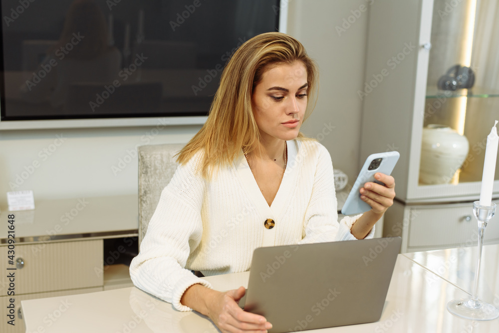 Young beautiful woman works for a computer from a home with a laptop on a white desk as a freelancer. Young businesswoman talking on the phone while working from home Young beautiful woman works for a computer from a home with a laptop on a white desk as a freelancer. Young businesswoman talking on the phone while working from home