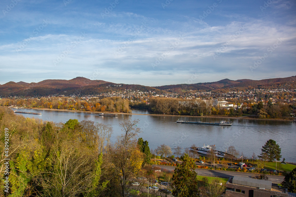 Top view at the river Rhine near to Rolandseck with river barges and a car ferry, trees in foreground and hills in background