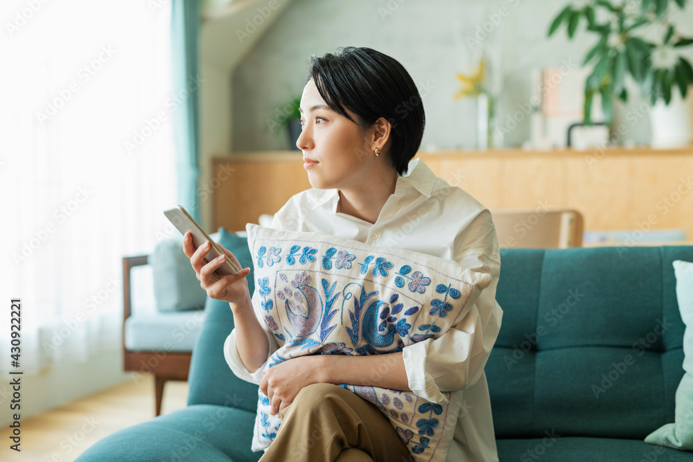© One - リビングでスマートフォンを見る女性