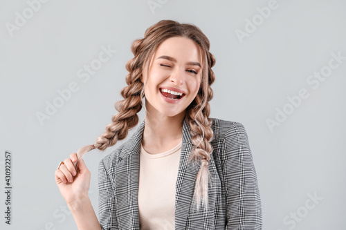 Beautiful young woman with braided hair on grey background