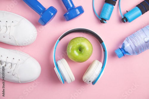 Fitness equipment. Dumbbells, apple, headphones, water bottle on pink background.