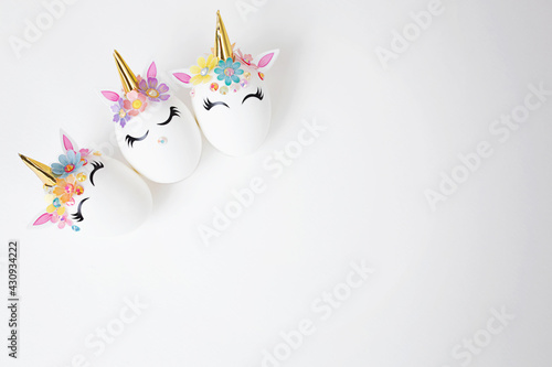 Three Easter eggs decorated with unicorn stickers on a white background. Copy space. Top view. Background for Easter.