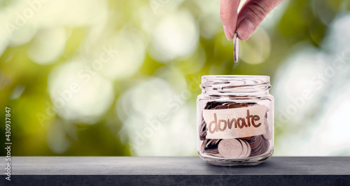 Hand putting coins in glass and have words donate write on label. Giving and donation concept.