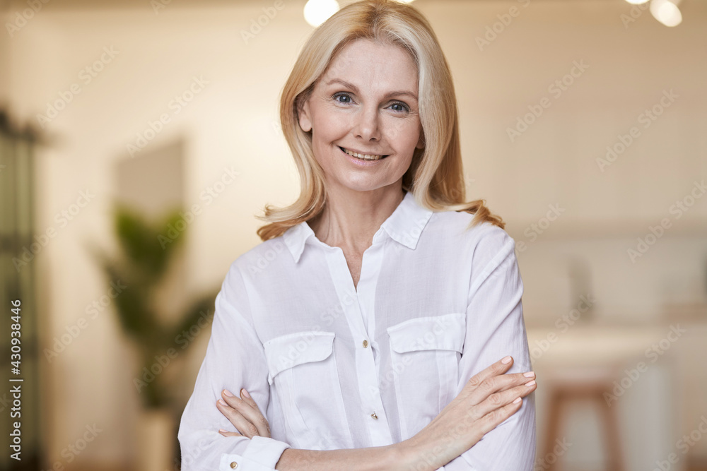 Elegance. Portrait of kind mature woman wearing white shirt smiling at camera while posing indoors
