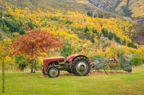 An old tractor in a field, with a hillside covered in bright autumn foliage behind. Photographed at Arthurs Point, South Island, New Zealand