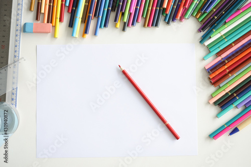 Red pencil lying on blank sheet of paper among multicolored