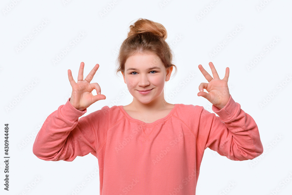 Portrait of a cute young girl in pink casual sweatshirt showing OK gesture with both hand. White background Portrait of a cute young girl in pink casual sweatshirt showing OK gesture with both hand. White background