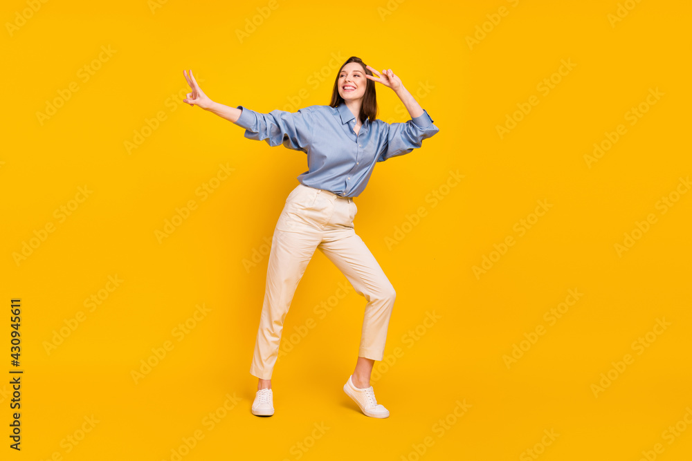 Photo of funny cute young lady dressed blue outfit showing v-signs dancing isolated yellow color background