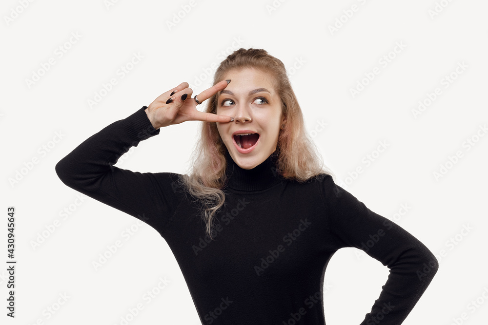 Attractive young woman showing v-sign near eye and gazing happy at camera, staying positive Attractive young woman showing v-sign near eye and gazing happy at camera, staying positive