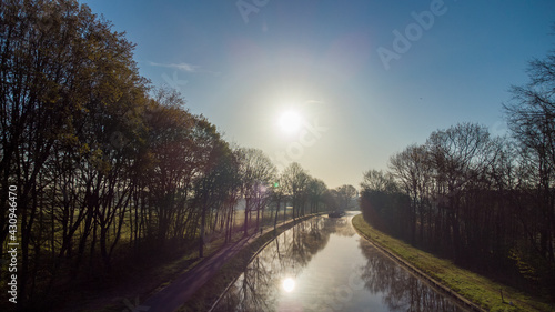Aerial view of an Idillic river stream canal with grass banks and wild flowers and trees in a scenic landscape on a misty sunny spring morning sunrise day, taken with a drone. High quality photo