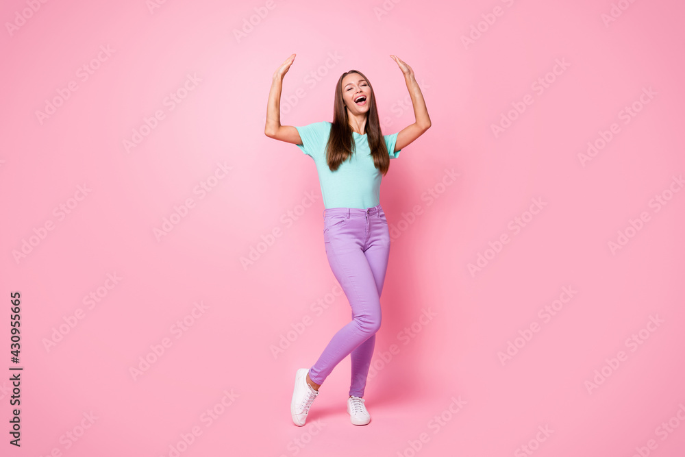 Full size photo of young happy excited good mood woman dancing raise hands up isolated on pink color background Full size photo of young happy excited good mood woman dancing raise hands up isolated on pink color background