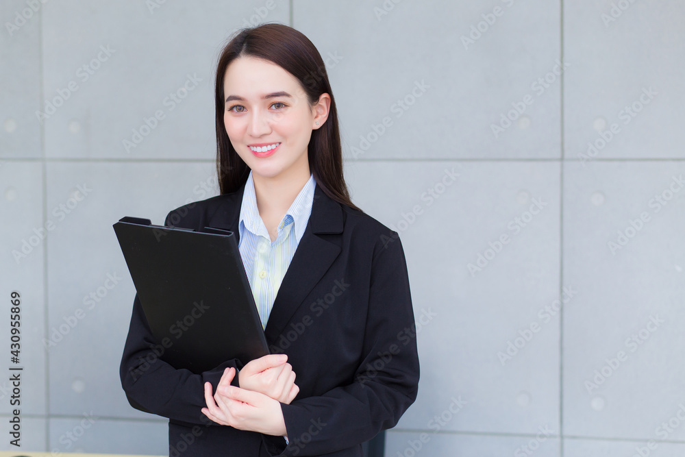 Asian business woman in black suit smiles happily while she works and holds clipbroad in office. Asian business woman in black suit smiles happily while she works and holds clipbroad in office.