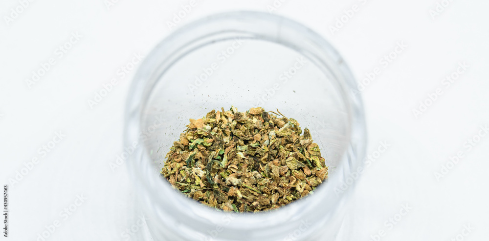 Ground buds of medical marijuana stored in plastic jar. Closeup on medical hemp blend isolated on white background. CBD, medical hemp in container. Ground buds of medical marijuana stored in plastic jar. Closeup on medical hemp blend isolated on white background. CBD, medical hemp in container.