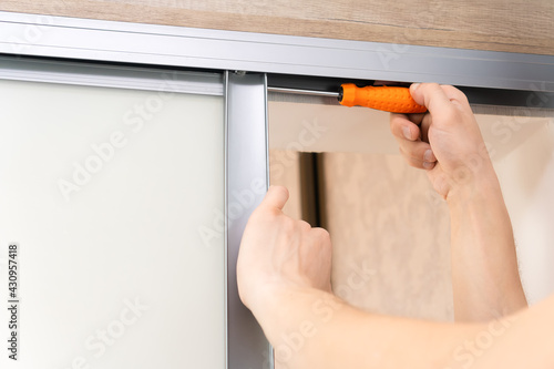 Close up of the hands of a male repairman with a screwdriver fixing a sliding door