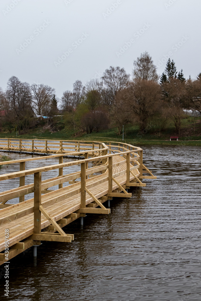 Naklejka premium A new wooden boardwalk above the pond water, dark waves, cloudy skies.