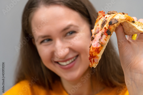 Close-up of a beautiful, happy, smiling young woman holding a slice of pizza in her hand and looking at it with adoration close-up. Focus on pizza