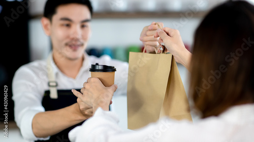 Close up hand. Asian young man or bartender serving paper bag and paper coffee glass customer at coffee shop. making coffee in coffee cafe. Concept sale paper bag and coffee. 