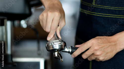 close up photo of male hands holding a metal tamper and a portafilter with coffee in a coffee shop. A man barista preparing for pressing ground coffee for brewing espresso or americano in a cafe.