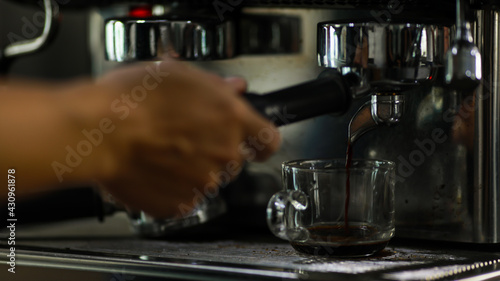 Close up shot of glass cup filled with hot delicious good smell black coffee made by barista hand from luxury coffee making machine in cafe with blurred foreground and background