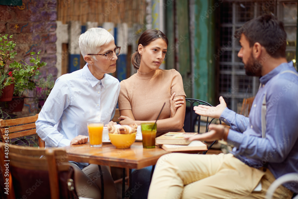 The young man defends himself from a verbal attack by his female friends of different generations while they having a drink at a bar. Leisure, bar, friendship, outdoor The young man defends himself from a verbal attack by his female friends of different generations while they having a drink at a bar. Leisure, bar, friendship, outdoor