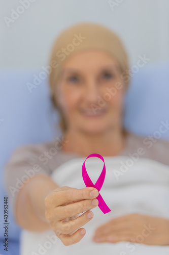 A middle-aged breast cancer patient lay on the bed and showing the pink ribbon symbol of breast cancer © Bangkok Click Studio