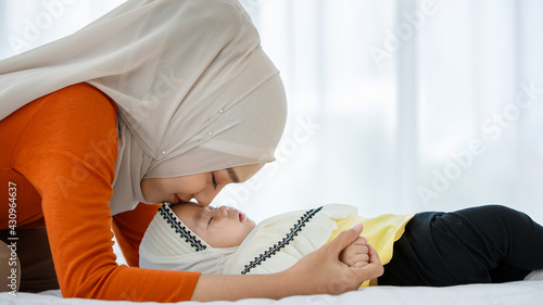 A cute and beautiful Asian Muslim in hijab dress kissing her baby daughter with a tender gesture. Love, care, and relationship concept