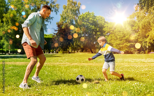 family, fatherhood and people concept - happy father and little son with ball playing soccer at summer park