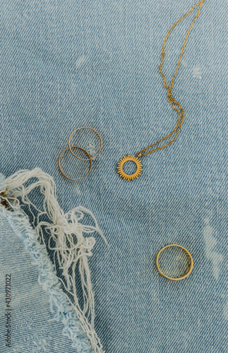 Bodegón con joyas de oro sobre tejido denim azul claro con manchas blancas y flecos deshilachados photo