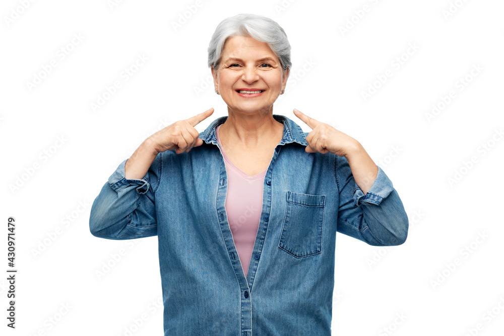 old people concept - portrait of smiling senior woman in denim shirt pointing fingers to her face over white background old people concept - portrait of smiling senior woman in denim shirt pointing fingers to her face over white background