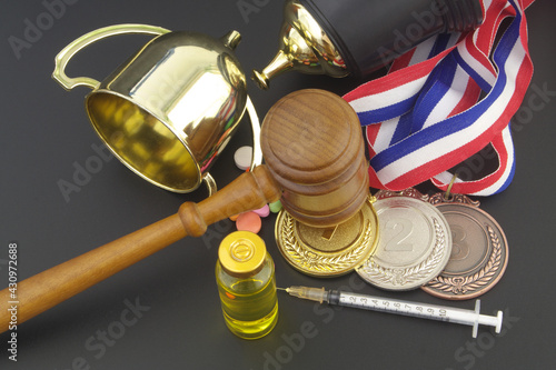 Broken golden winner cup with doping pills, syringe, medals and gavel as justice symbol on table, doping in sport concept.