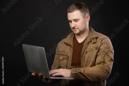 A portrait of a focused Caucasian man with a laptop in his hands stands in the studio and looks attentively into the laptop. The concept of using pc and mobile remote access to services