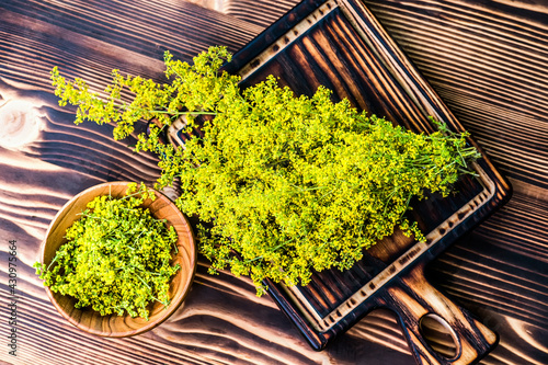 Galium verum, lady bedstraw or yellow bedstraw used in alternative medicine in wooden plate on a vintage table next utting boards. Medicinal herbs Hypericum for Homeopathic Remedies photo