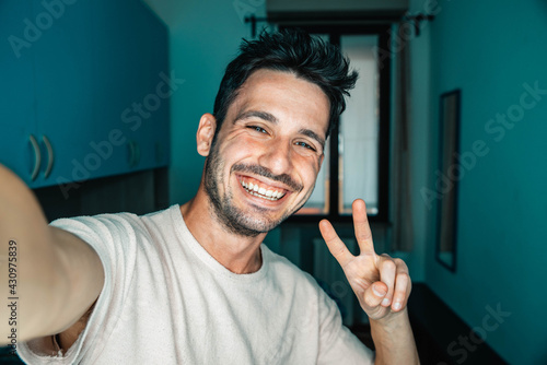 Happy young man taking a selfie at home - Smiling guy looking at camera indoor - People and technology concept