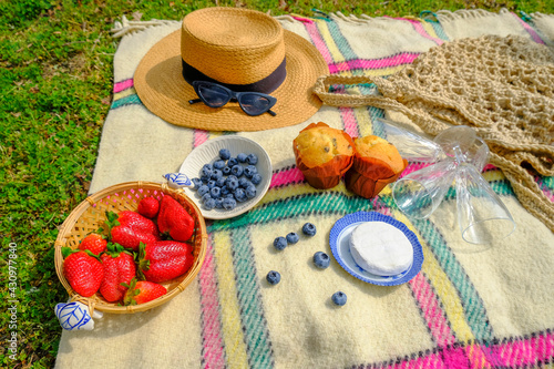 still life ripe strawberries, straw hat, sunglasses, empty glasses, brie cheese, and pastry on checkered plaid. top view. summer picnic in the park	
