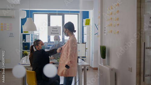 Two coworkers touching elbow during coronavirus global pandemic while working at business project wearing medical face mask to prevent infection with virus disease. Company mantain social distancing photo